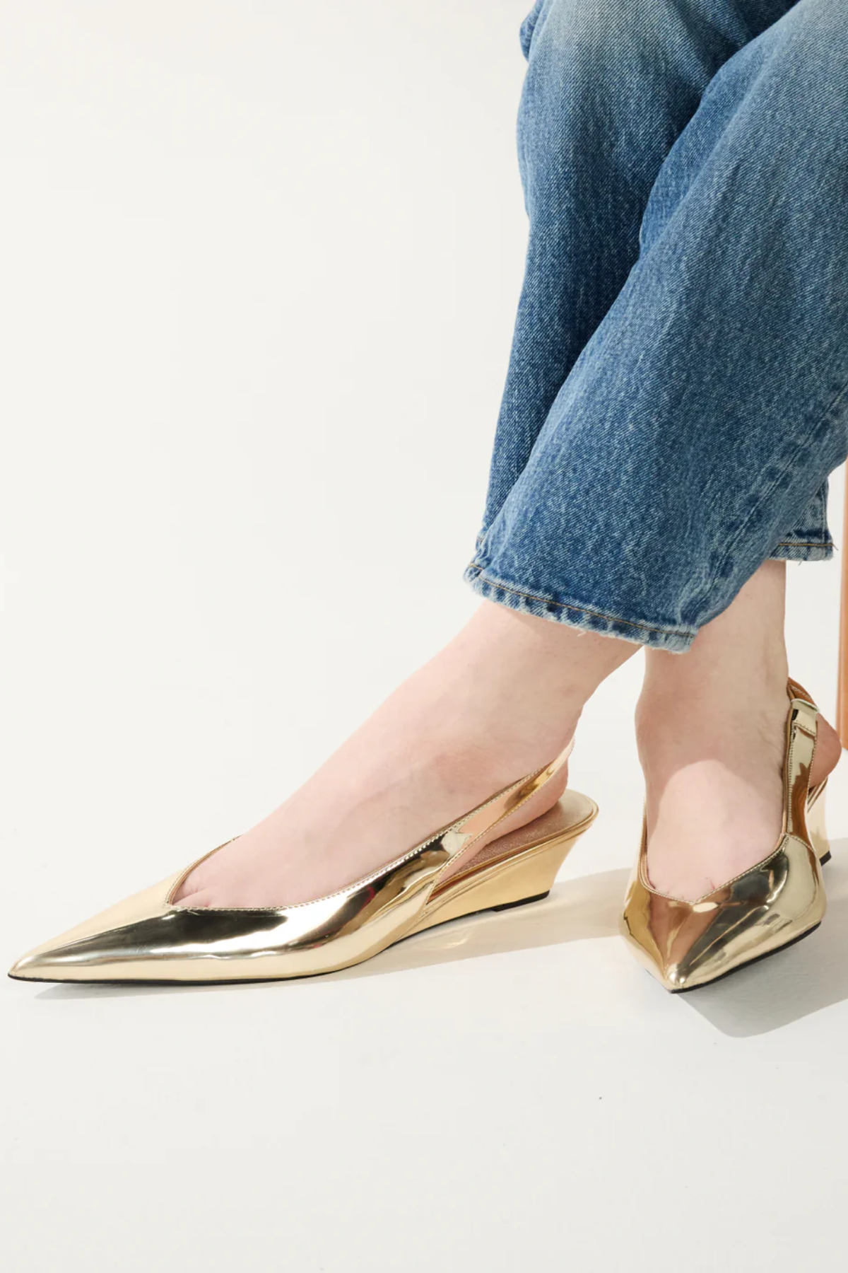 Gold pointed-toe shoes worn with blue jeans on a light background