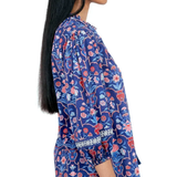 A woman shown in side profile wearing a blue floral blouse with red and pink flowers, paired with light blue jeans, against a plain white background.