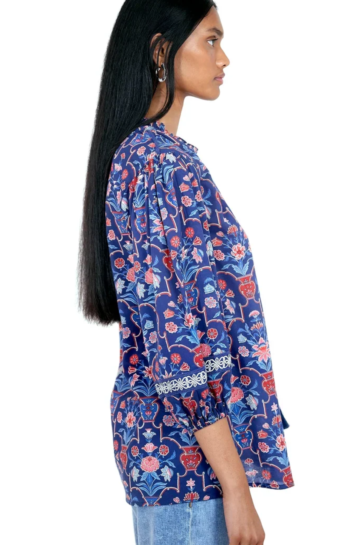 A woman shown in side profile wearing a blue floral blouse with red and pink flowers, paired with light blue jeans, against a plain white background.