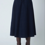 A dark navy blue A-line midi skirt with an elastic waistband, shown on a model from the back wearing brown high-heeled boots against a light gray studio background.