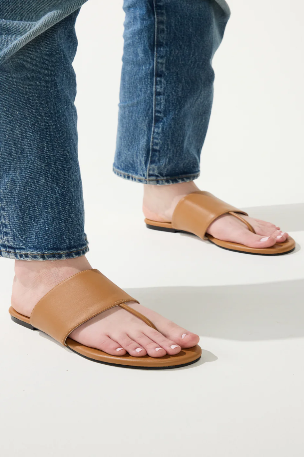 Tan sandals worn with blue jeans on a light background