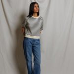 Person wearing a striped sweater and blue jeans against a plain background