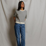 Person wearing a striped sweater and blue jeans against a plain background