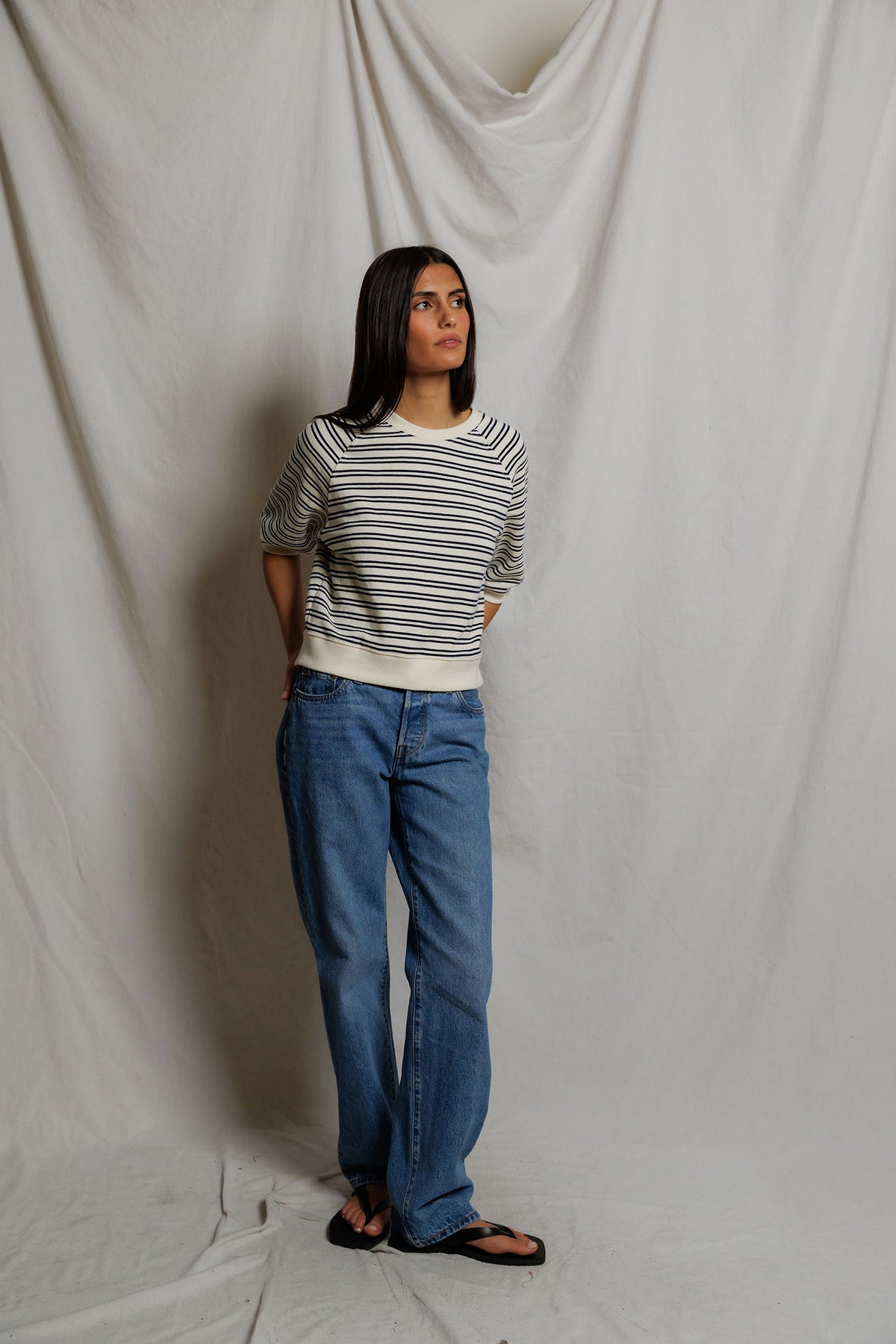 Person wearing a striped sweater and blue jeans against a plain background