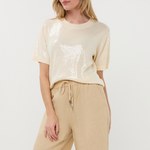 Woman wearing a beige sequin top and beige pants on a white background