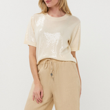 Woman wearing a beige sequin top and beige pants on a white background