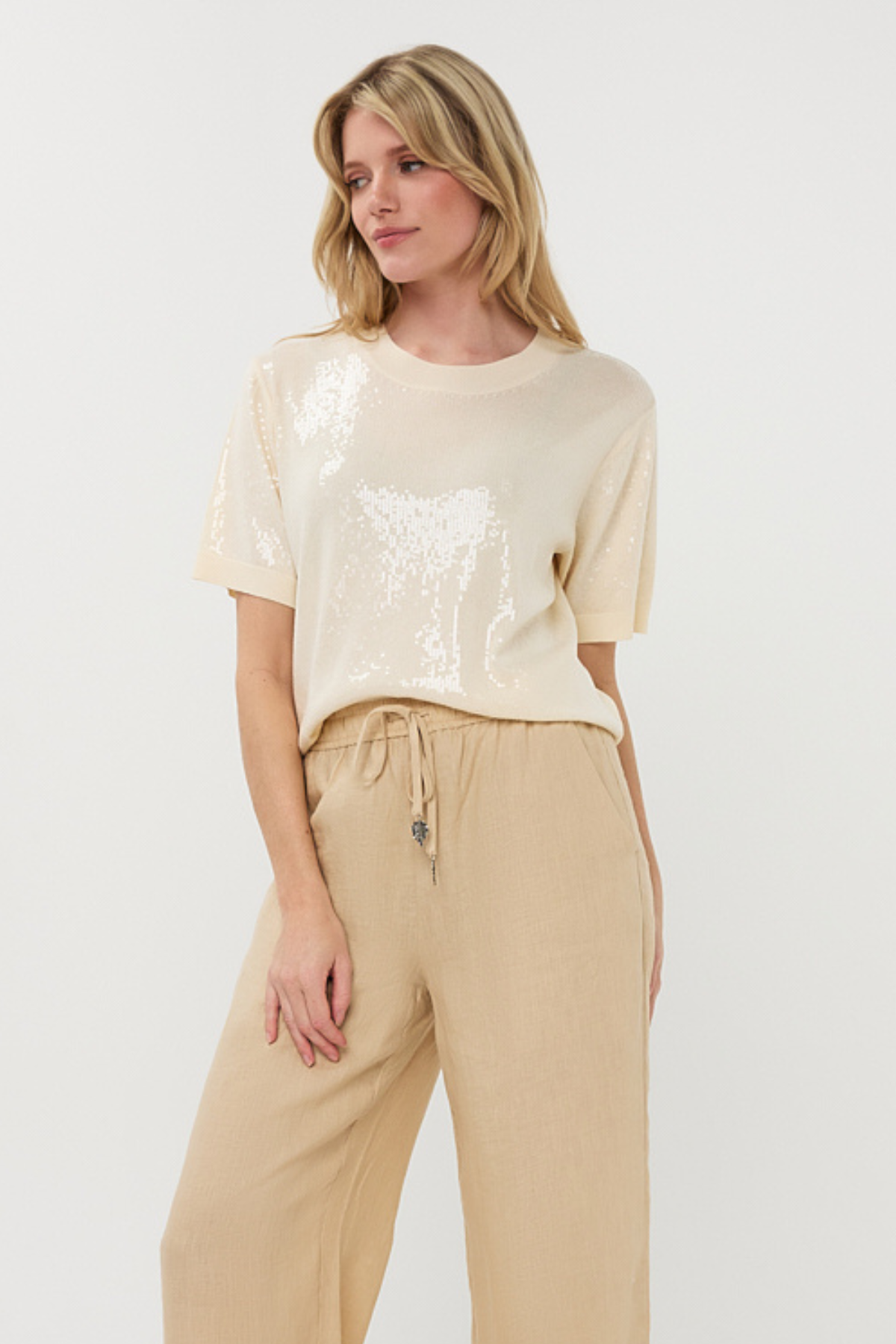 Woman wearing a beige sequin top and beige pants on a white background