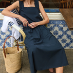 Woman in a navy dress sitting outdoors with a wicker bag.