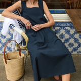 Woman in a navy dress sitting outdoors with a wicker bag.