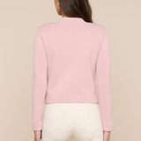 Person wearing a pink long-sleeve top and white pants on a beige background
