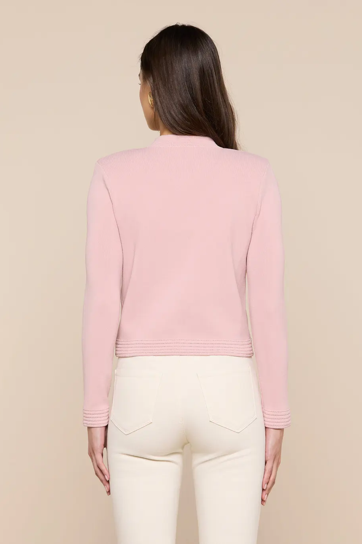 Person wearing a pink long-sleeve top and white pants on a beige background