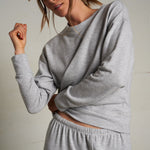 Woman wearing a light grey long-sleeve knit top with a relaxed fit, photographed against a soft neutral backdrop.