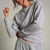 Woman wearing a light grey long-sleeve knit top with a relaxed fit, photographed against a soft neutral backdrop.