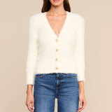 A woman modeling a fuzzy off-white cardigan sweater with a V-neck and three front buttons, paired with blue jeans, against a solid beige background.