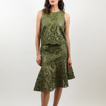 A woman modeling a sleeveless olive green midi dress with a textured, patterned surface and a ruffled hem, paired with brown slide sandals, against a plain light gray studio background.
