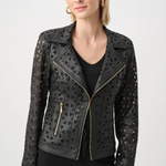 A woman wearing a black faux-leather moto jacket with geometric laser-cutout patterns and gold-tone zippers, paired with a black top and black pants, against a light gray studio background.