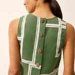 Woman wearing a green dress with white geometric patterns and buttons on a beige background