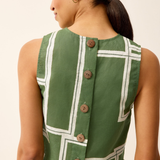 Woman wearing a green dress with white geometric patterns and buttons on a beige background