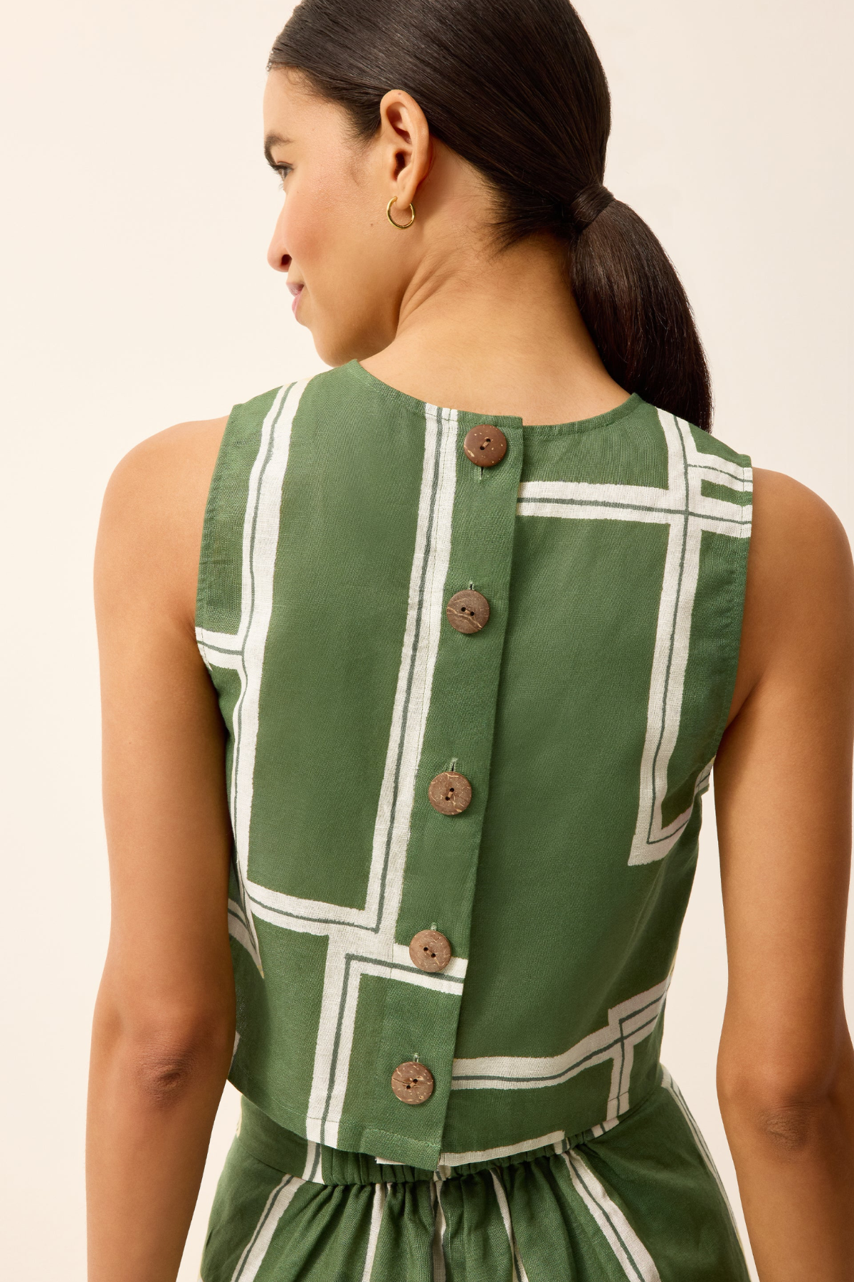 Woman wearing a green dress with white geometric patterns and buttons on a beige background