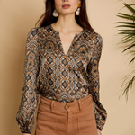Woman wearing a patterned blouse and brown pants against a beige background