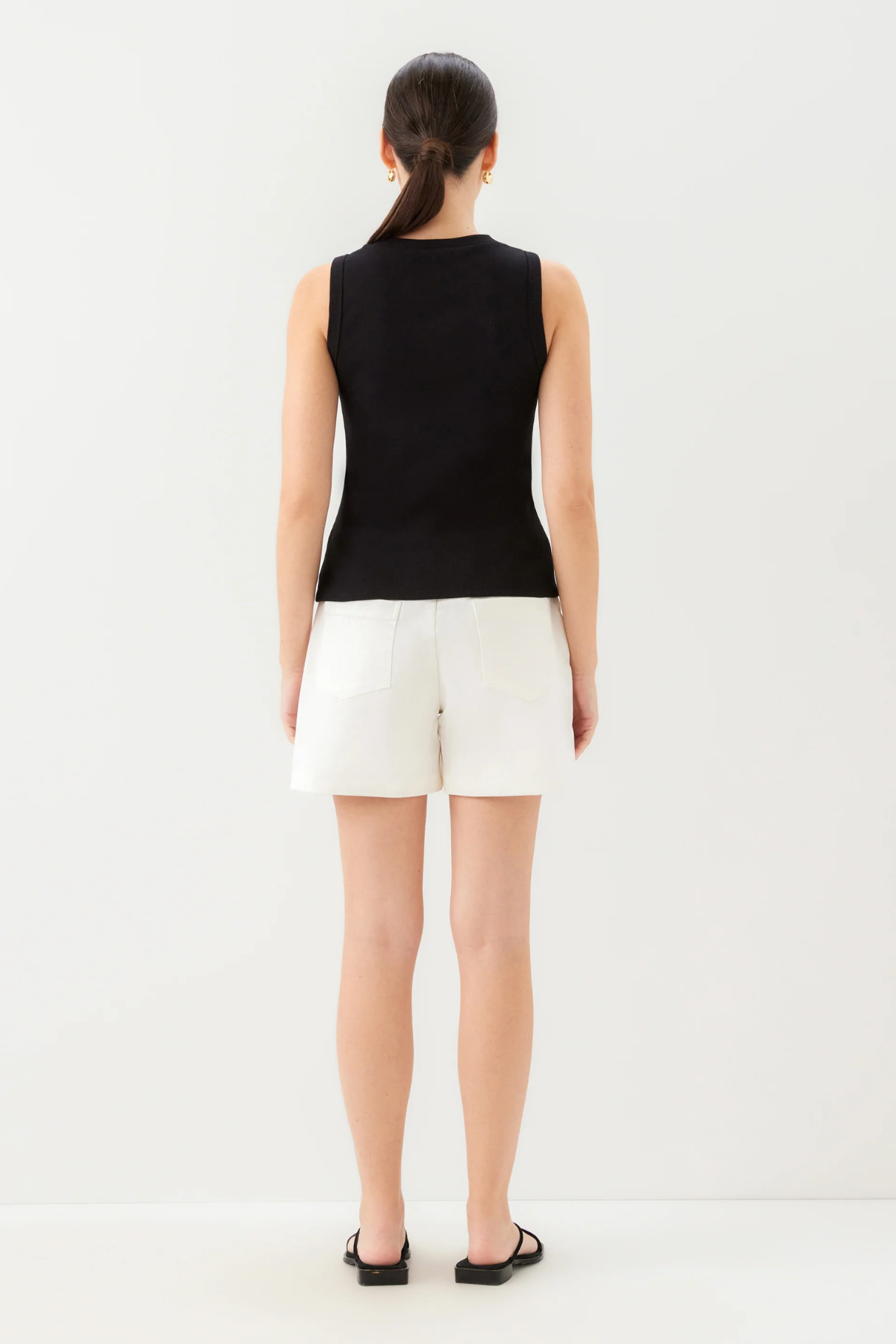 Woman wearing a black sleeveless top and white shorts on a white background