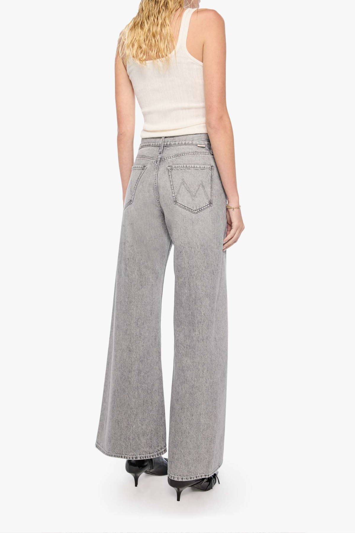 A woman shown from the back wearing light gray wide-leg denim jeans, a white ribbed tank top, and black heels against a plain white studio background.