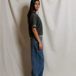 Person wearing a gray sweater and blue jeans standing against a plain white background
