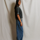 Person wearing a gray sweater and blue jeans standing against a plain white background