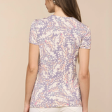 Woman wearing a patterned shirt and white pants on a beige background