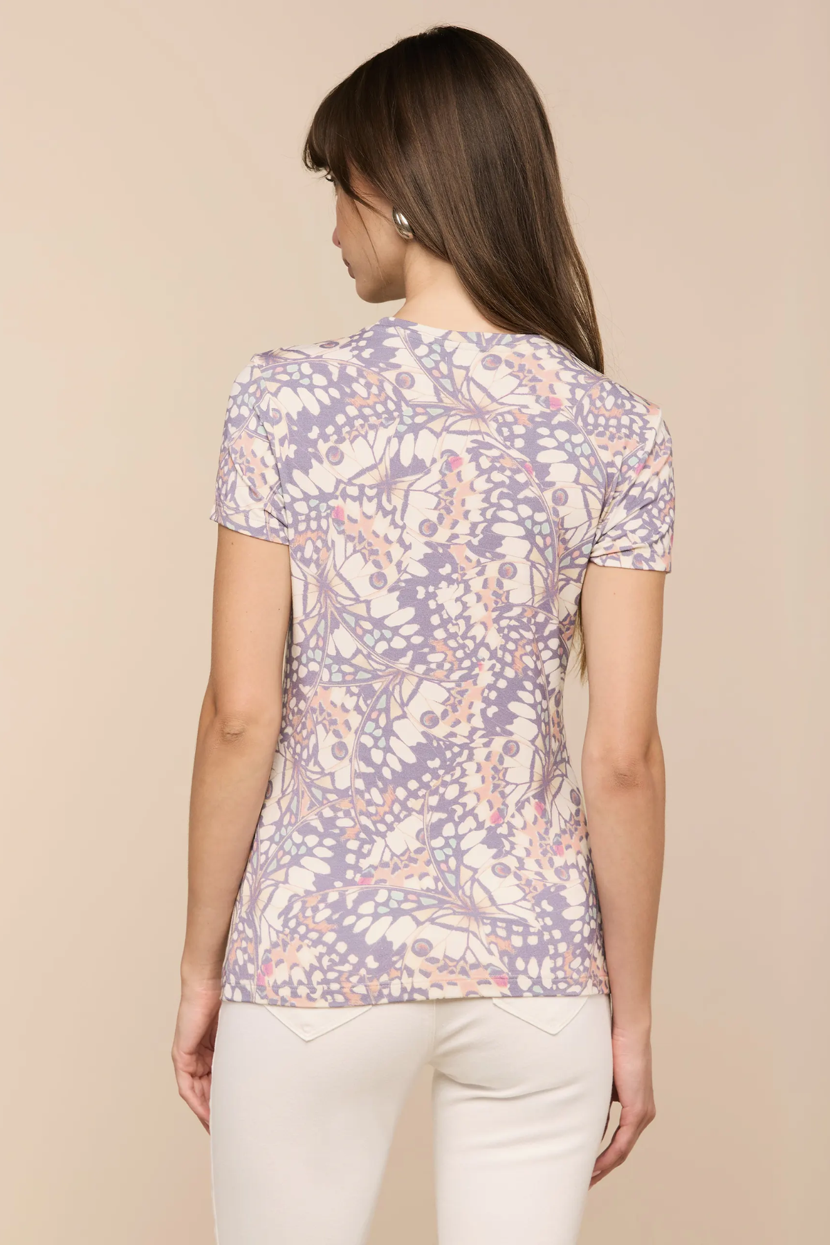 Woman wearing a patterned shirt and white pants on a beige background