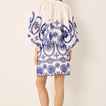 Woman wearing a white dress with blue floral patterns on a plain background