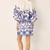 Woman wearing a white dress with blue floral patterns on a plain background