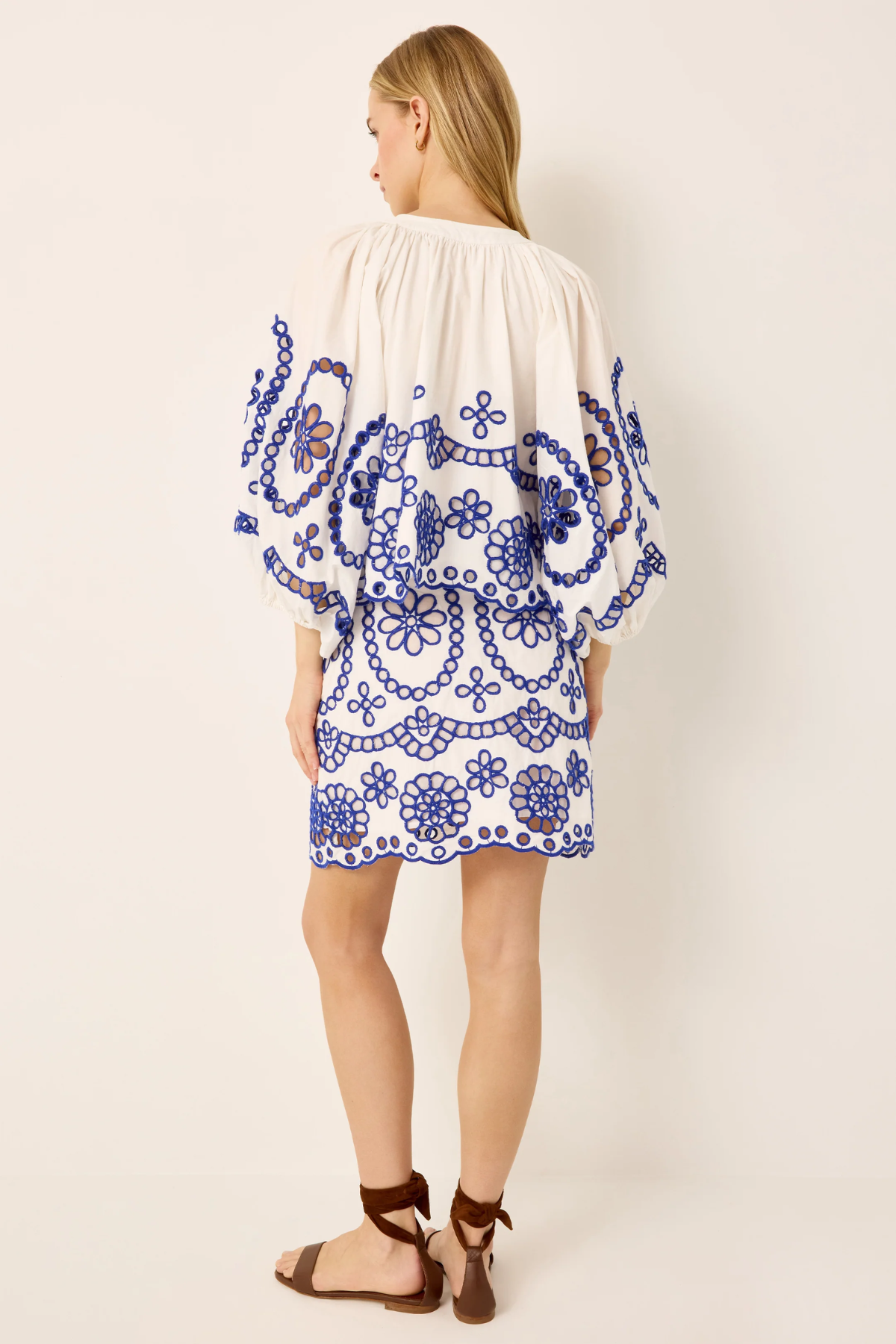 Woman wearing a white dress with blue floral patterns on a plain background