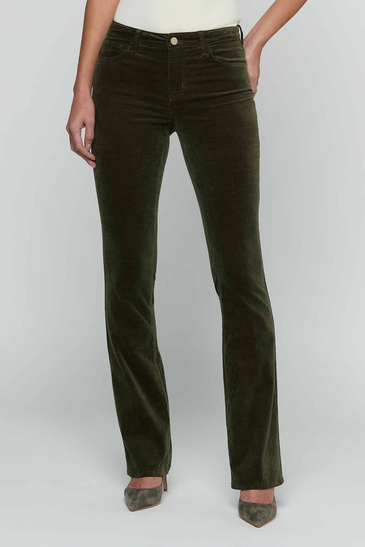 A model wearing dark olive green corduroy straight-leg jeans with a gold button closure, paired with gray pointed-toe heels, against a light gray studio background.