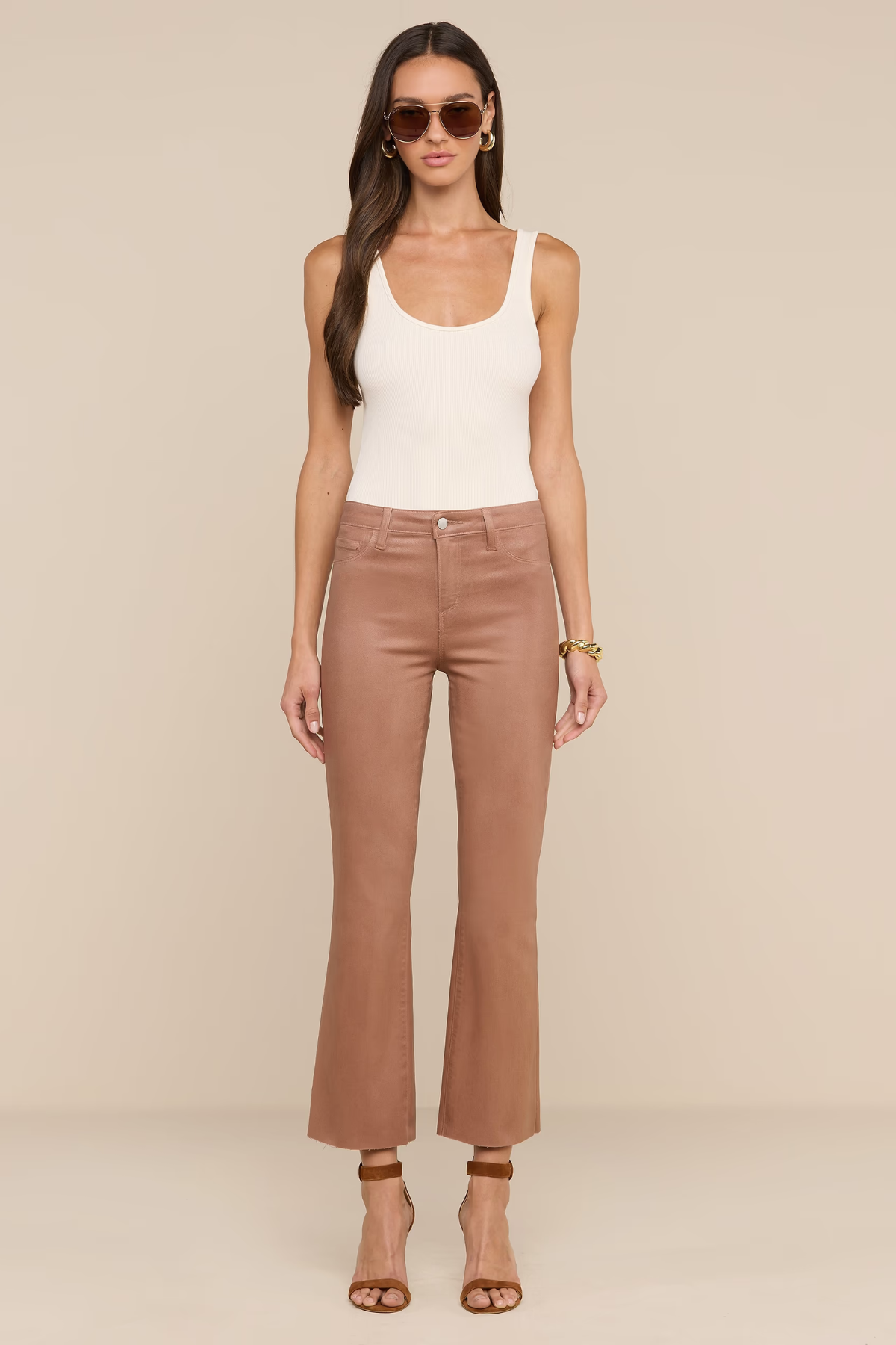 Model wearing white tank top and tan jeans on ivory background.