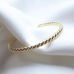 A gold-toned twisted rope cuff bracelet resting on draped white fabric.