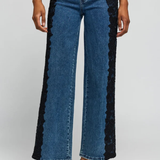 A model wears blue wide-leg jeans with black lace panels running down the outer sides, styled with a navy top and black heels against a light gray studio background.