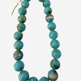 A beaded necklace made of round turquoise-blue marbled beads with a small gold clasp, shown on a plain light gray background.