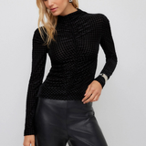 A woman modeling a black textured long-sleeve mock neck top paired with black faux leather pants, against a light gray studio background.