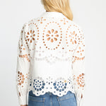 Woman wearing a white lace top with blue jeans on a light gray background