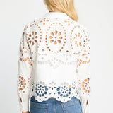 Woman wearing a white lace top with blue jeans on a light gray background