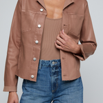 Model wearing a light-wash slim-fit denim jacket with raw hem detailing and a button-front design.