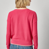 Person wearing a pink ribbed sweater and blue jeans on a plain background
