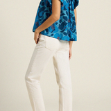back of woman in blue floral blouse and white pants on tan background 