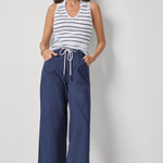Woman wearing a striped tank top and blue wide-leg pants on a plain background