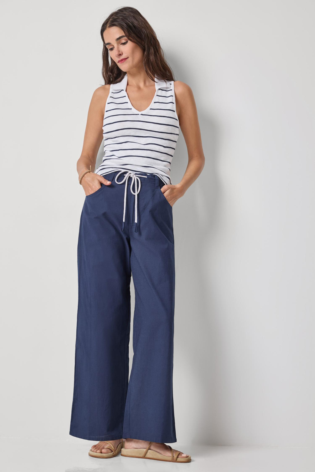 Woman wearing a striped tank top and blue wide-leg pants on a plain background