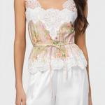 Woman wearing a white lace top with floral design and white pants on a plain background