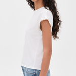 A woman wearing a white short-sleeve t-shirt with delicate scalloped edges on the sleeves, paired with light blue jeans, shown from a side profile against a plain white background.