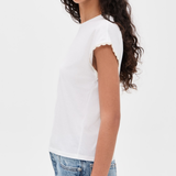 A woman wearing a white short-sleeve t-shirt with delicate scalloped edges on the sleeves, paired with light blue jeans, shown from a side profile against a plain white background.