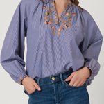 Woman wearing a blue blouse with floral embroidery and blue jeans on a white background